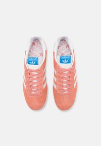 Adidas superge iz mehkega koralne sued kože z belimi črtami. Imajo vezalni dizajn, teksturirano zgornji del in logo na jeziku.