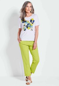 Witte t-shirt met bloemmotief en blauwe en gele accenten, gecombineerd met felgroene broek, met een ontspannen pasvorm en zachte textuur.