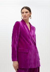 Fuchsiavävd kavaj med dubbelknäppt design, slipskrag och strukturerade axlar. Har framfickor och subtil ribbad textur.