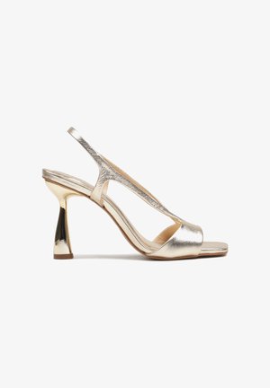 Złoty metaliczny sandał na wysokim obcasie typu slingback z kwadratowym otwartym noskiem i rozszerzanym, masywnym obcasem.