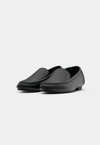 Black leather loafers with a smooth texture, rounded shape, and minimalistic design. Features a low heel and stitched detailing on the edges.