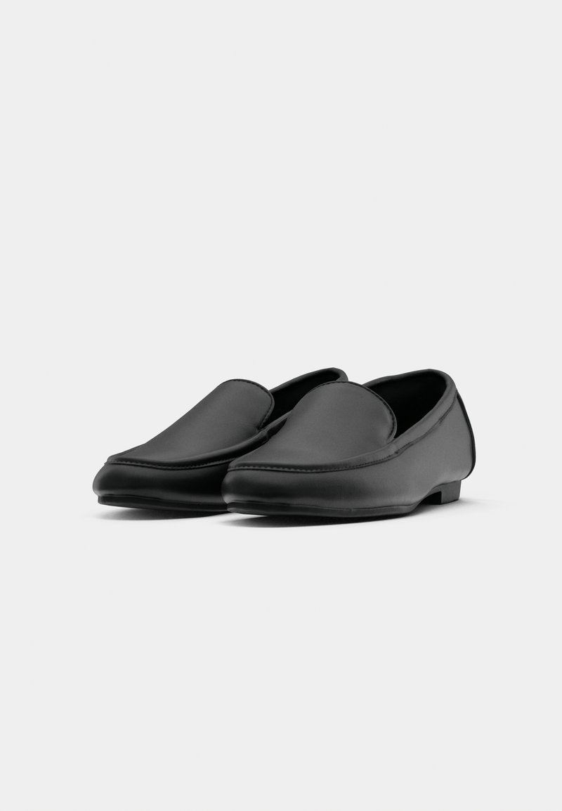 Mocassins en cuir noir avec une texture lisse, une forme arrondie et un design minimaliste. Présentent un talon bas et des détails cousus sur les bords.