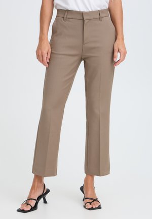 Pantalones beige de pierna recta usados con sandalias negras de tacón con tiras en una persona de pie sobre un fondo blanco.