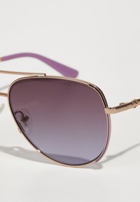 Aviator prillid kuldse metallraami ja gradient-lillade läätsedega. Päikeseprillide varred on ühtlaselt lillad. Minimalistlik bränding on nähtav.