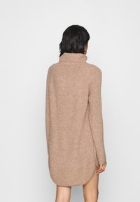 Robe pull en tricot beige doux, dotée d'un col montant, de manches longues et d'un ourlet arrondi, avec une coupe décontractée et une finition texturée.