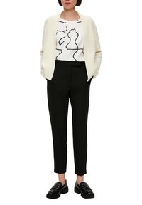 Crème vest, witte blouse met zwarte abstracte patronen, zwarte op maat gemaakte broek en zwarte loafers. Over het algemeen een eenvoudige en gestructureerde look.