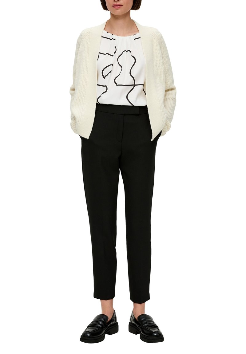 Crème vest, witte blouse met zwarte abstracte patronen, zwarte op maat gemaakte broek en zwarte loafers. Over het algemeen een eenvoudige en gestructureerde look.