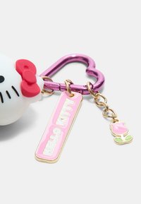 Breloczek z figurką białego kotka Hello Kitty w czerwoną kokardą, różową zawieszką z napisem "HELLO KITTY" oraz małym różowym różą ozdobioną złotymi akcentami.