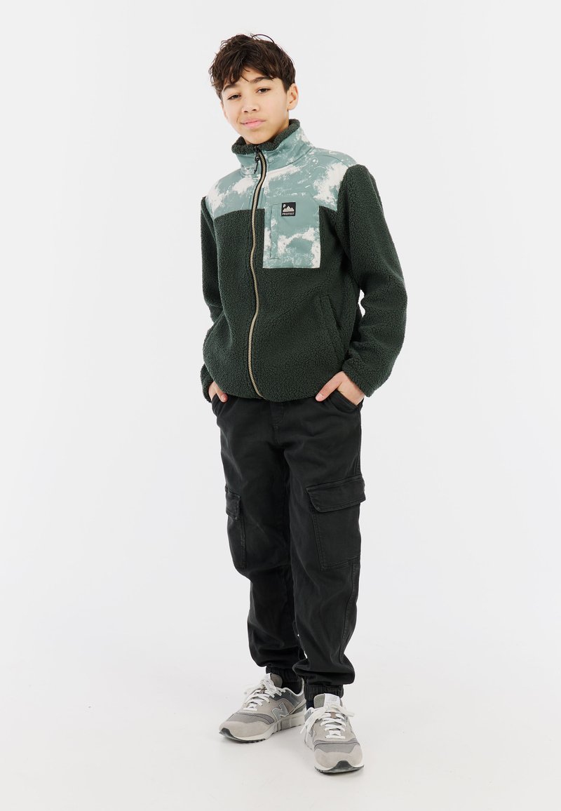 Groene fleecejas met een lichtgroene en witte gestreepte bovenkant, rits sluiting en een borstzakje aan de linkerkant. Gepaard met zwarte cargobroek.