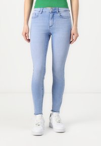 Light blue skinny jeans with a mid-rise waist, five pockets, and subtle fading details, paired with white sneakers.