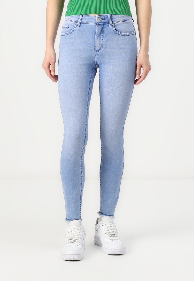 Light blue skinny jeans with a mid-rise waist, five pockets, and subtle fading details, paired with white sneakers.