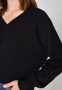 Pull noir à col en V, à coupe ample, avec des manches longues et des poignets côtelés. Fabriqué en tissu doux et texturé, mettant en valeur une surface lisse.