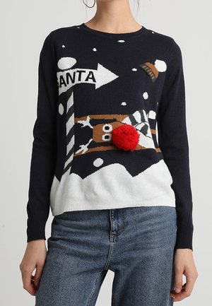 Pull bleu marine avec de la neige, un panneau indiquant la direction du Père Noël et un renne avec un gros pompon rouge sur le nez, porté avec un jean bleu.