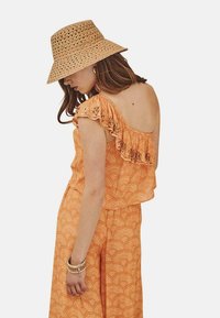 Vestido naranja con estampado y escote con volantes, combinado con un sombrero de paja tipo cubo. Presenta un diseño sin espalda y corte holgado.