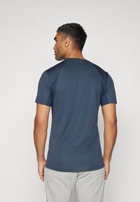 Camiseta atlética de manga corta en azul marino con cuello redondo y tela texturizada. Muestra un diseño en la parte posterior y un estilo ajustado.