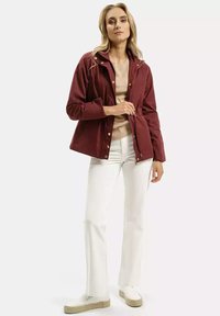 Bordowa kurtka typu soft-shell z regulowanym w pasie, zapinana na zamek błyskawiczny i zatrzaski, w połączeniu z beżową bluzką i białymi spodniami.