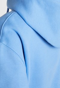 Felpa blu chiaro con tessuto morbido e strutturato. La vista ravvicinata mette in evidenza le cuciture e la forma del cappuccio. Design minimalista.