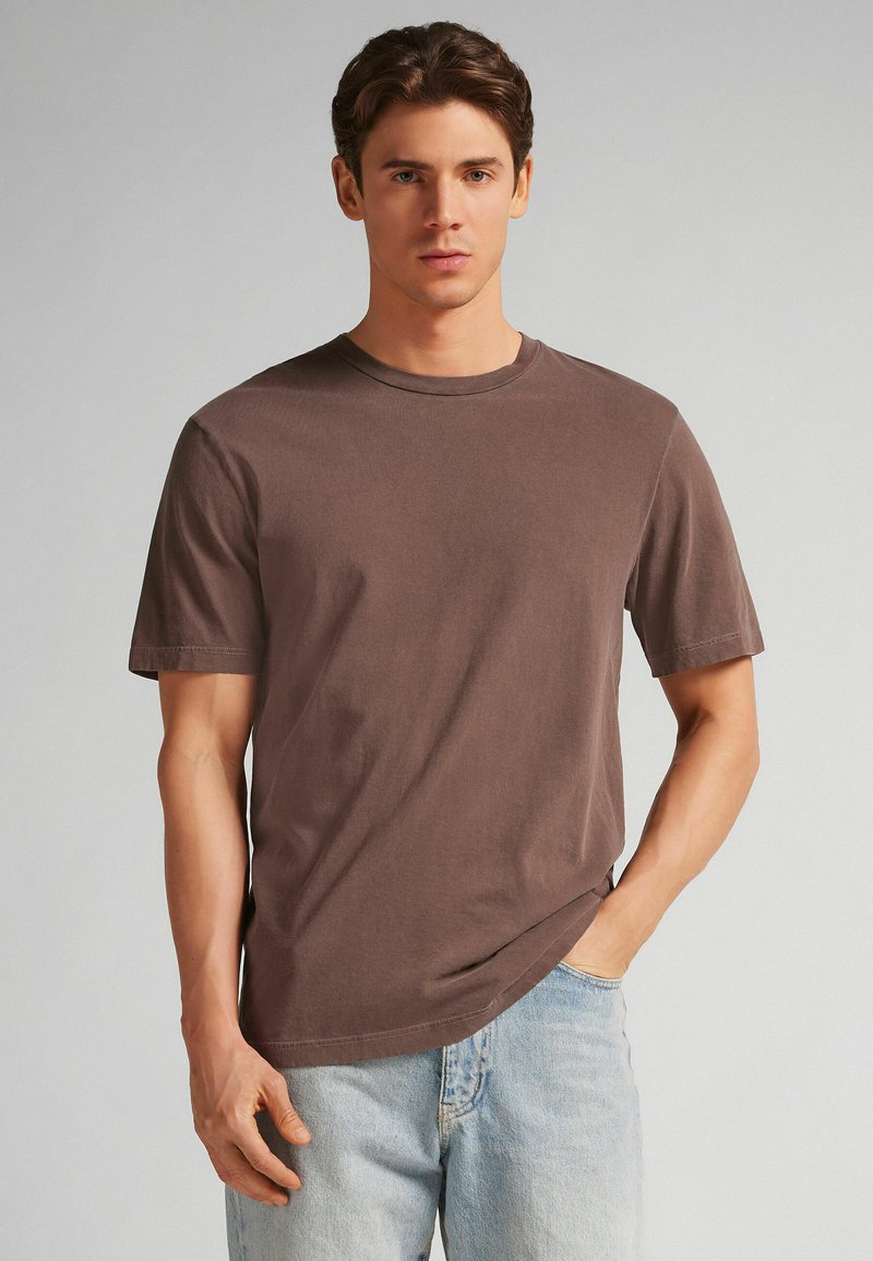 Hnědé bavlněné tričko s krátkým rukávem, kulatým výstřihem a uvolněným střihem, doplněné o světle modré džíny.