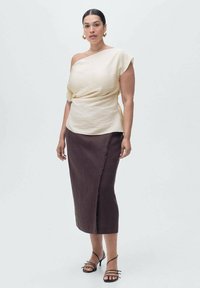 Haut crème asymétrique en tissu texturé, associé à une jupe ajustée marron foncé avec une bordure brut. Accentué par des talons à lanières.