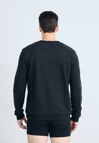 Sudadera negra de manga larga, con cuello redondo y puños acanalados, llevada sobre pantalones cortos negros. Diseño simple sin patrones visibles.