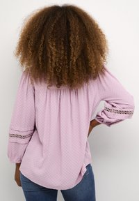 Blusa viola chiaro con un motivo texturizzato, vestibilità ampia, schiena arricciata e dettagli in pizzo aperto sulle maniche. Stile casual.