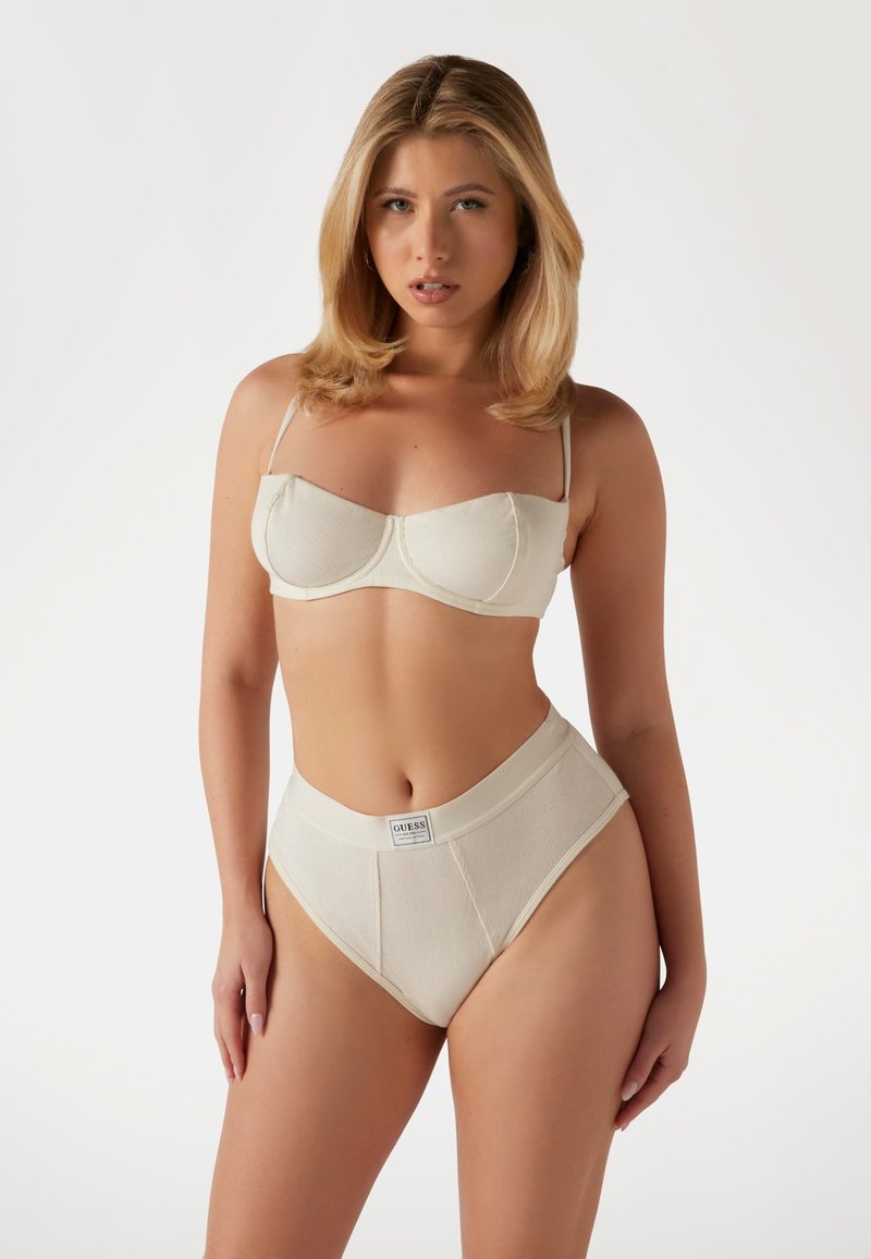 Beige geribbelde bh en hooggesneden ondergoed set, met verstelbare bandjes en een logo label op de tailleband. Gladde textuur overal.