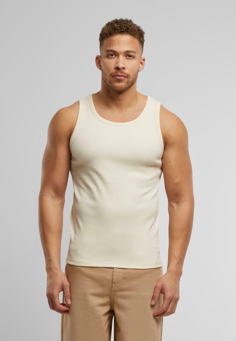 Beige gerippter Tanktop mit rundem Ausschnitt, in figurschmeichelndem Design und breiten Schulterträgern, kombiniert mit hellbraunen Hosen.