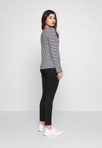 Top de mangas longas às riscas pretas e brancas com colarinho vermelho, combinado com leggings pretas e ténis brancos. Riscas verticais por todo o lado.