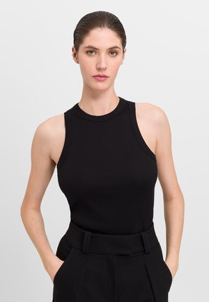 Black ribbed tank top with round neck and wide shoulder straps, paired with high-waisted black tailored pants. Smooth texture, fitted design.