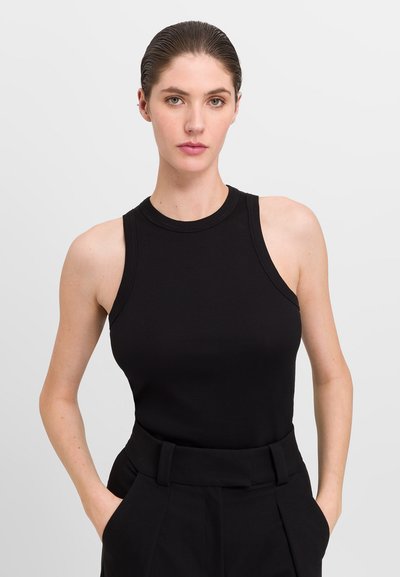 Débardeur noir à côtes avec col rond et larges bretelles, associé à un pantalon tailleur noir taille haute. Texture lisse, design ajusté.
