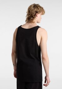 Musta toppi, joka on valmistettu puuvillasta, ja jossa on pyöreä kaula-aukko sekä hihaton muotoilu. Takana on hieman pidempi helma.