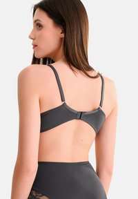 Soutien-gorge gris avec bretelles réglables, présentant une texture de tissu lisse et une fermeture à crochets au dos. Conception minimaliste, sans motifs.