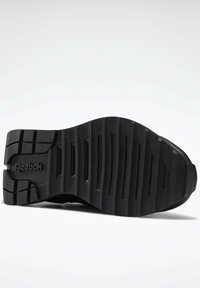 Suola di sneaker in gomma nera con un motivo scanalato, logo "Reebok" in rilievo e finitura liscia. Nel complesso, presenta un design robusto e testurizzato.