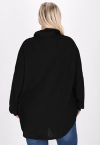 Camicia nera oversize con tessuto testurizzato, maniche lunghe e vestibilità ampia. Presenta un colletto rotondo e un orlo curvo.