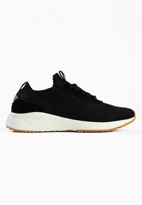 Black athletic shoes with a breathable knit upper, textured details, round toe, and a white midsole. Features a lightly gripped gum rubber outsole.