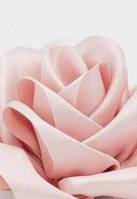 Vaaleanpunainen satiiniraitakukka, jossa on kerroksittain asetellut terälehdet, sileä pinta, pehmeä kiilto ja pyöreä muoto, joka esittelee herkkiä taitoksia ja lempeitä kaaria.