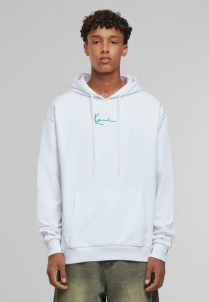 White hoodie with drawstrings and a kangaroo pocket, featuring green embroidered text on the chest, worn over light green jeans.