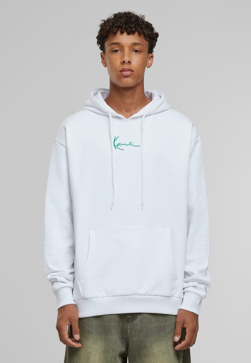 Sudadera blanca con cordones y un bolsillo tipo canguro, con texto bordado en verde en el pecho, llevada sobre unos jeans verde claro.