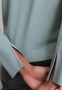 Licht teal, langemouwen trui met geribbelde boorden en een elegante zijsplit. Zachte stof met een comfortabele pasvorm.