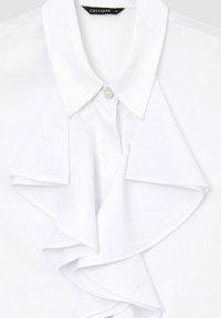 Blusa bianca con un design frontale a volant, dotata di colletto classico e un bottone decorativo al collo. Tessuto morbido e liscio.