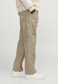 Pantalones cargo beiges con bolsillos laterales, diseño de pierna recta, fabricados en tejido ligero. Se llevan con zapatillas blancas.