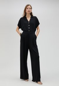 Mono negro con diseño de mangas cortas y cuellos, con botones en la parte delantera, silueta de pierna ancha y bolsillos, hecho de tela suave.
