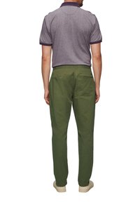 Vue de dos d'un homme : polo gris avec des bordures violettes, pantalon vert avec une taille élastique et une texture lisse, coupe décontractée.