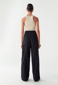 Bež ribana tank top v kombinaciji s prostornimi črnimi širokimi hlačami. Tkanine se zdijo mehke z gladko teksturo in minimalističnim dizajnom.