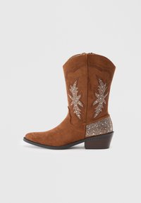 Brūni zamšveida kovboju zābaki ar norādītu purngalu, dekoratīvām izšuvumiem, lapu rakstiem un rotātu papēdi, kas rotāts ar rhinestones un pērlītēm.