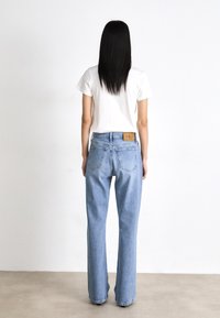 Vaqueros de mezclilla azul claro con corte recto, que presentan una etiqueta de cuero en la cinturilla trasera y dos bolsillos traseros. Camiseta blanca.