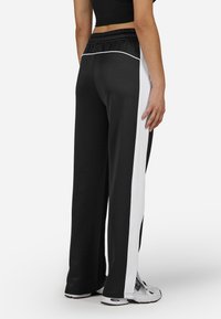 Calças largas pretas com riscas laterais brancas, em tecido texturizado e com um cós elástico. Combinadas com sapatilhas brancas.