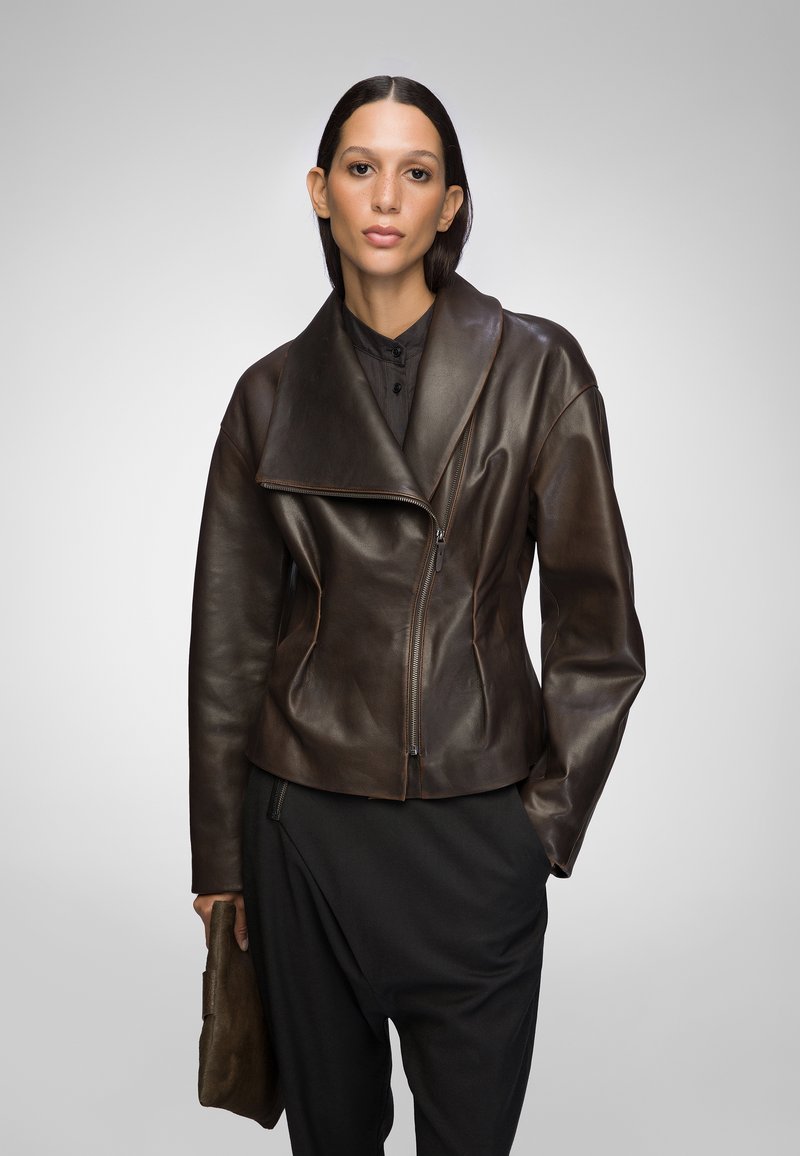 Brown leather jacket with a wide collar and asymmetrical zipper. Smooth texture, fitted design, accented with subtle stitching details.