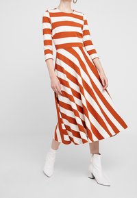 Robe A-line à manches longues avec des rayures verticales orange et blanches, fabriquée dans un tissu doux, dotée d'un col rond et d'une jupe évasée.