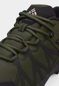 Πράσινο και μαύρο παπούτσι πεζοπορίας Columbia με υφασμάτινο δίχτυ, κορδόνια που διασταυρώνονται και επωνυμία στην γλώσσα.